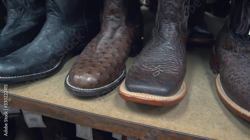 Cowboy boots in a store. Close-up of new cowboy boots on shelf. Aligned cowboys boots on a shelf in a store. Ostrich and crocodile leather cowboy boots lined up in a row in a retail store. photo