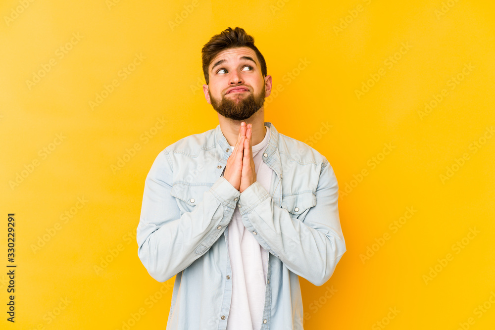 Young caucasian man isolated on yellow background holding hands in pray near mouth, feels confident. Young caucasian man isolated on yellow background holding hands in pray near mouth, feels confident.