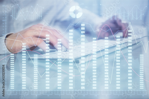 Double exposure of graph with man typing on computer in office on background. Concept of hard work. Closeup.