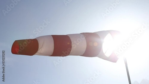 Side shot of red and white windsock blowing in wind with sun shining in background lens flare photo