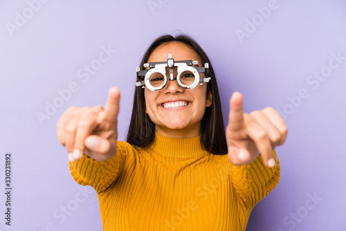Youn indian woman with optometry glasses cheerful smiles pointing to front.