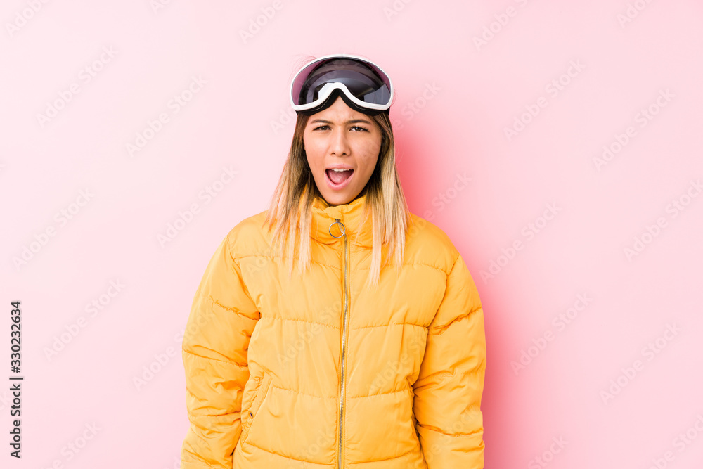 Young caucasian woman wearing a ski clothes in a pink background screaming very angry and aggressive. Young caucasian woman wearing a ski clothes in a pink background screaming very angry and aggressive.