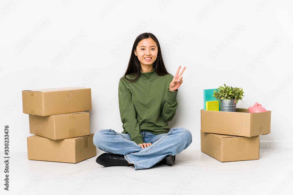 Young chinese woman moving to a new home showing victory sign and smiling broadly.