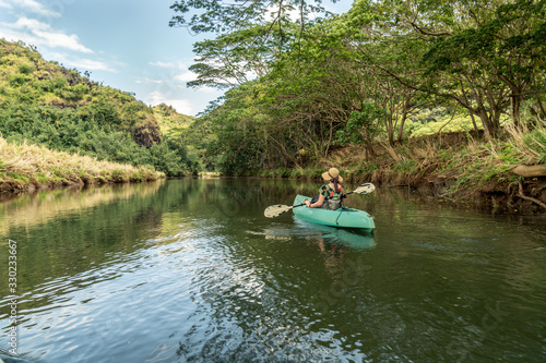Girl, woman, right, paddling a green kayak on a calm river with trees line the bank and puffy clouds in the sky, Wailua River, Kauai, Hawaii