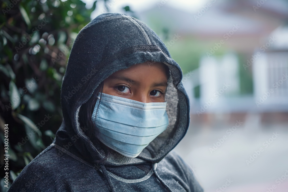 Latino 9 year old girl or student wearing a hoodie sweatshirt and medical face mask to prevent the spread of infectious diseases. Latino 9 year old girl or student wearing a hoodie sweatshirt and medical face mask to prevent the spread of infectious diseases.