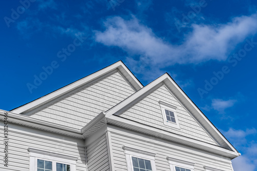 Double gable, with white decorative trim over the windows on a triangle gable roof, white soffit and fascia, colonial white horizontal vinyl lap siding with blue sky background