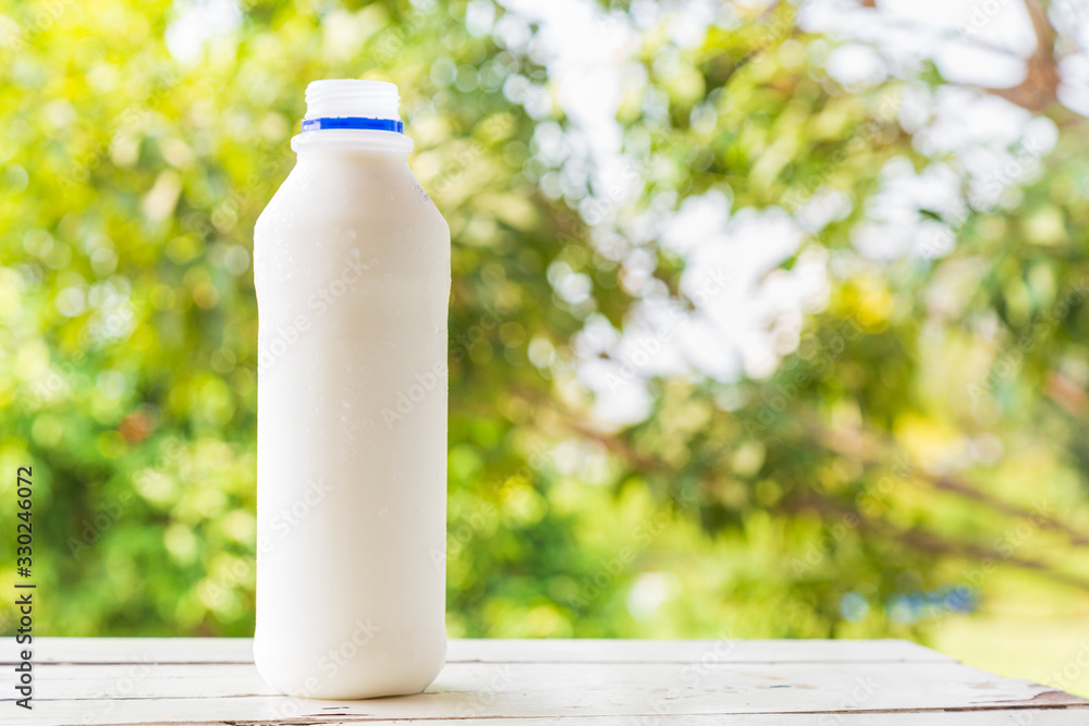Milk bottle on white wooden table with green nature background. Milk bottle on white wooden table with green nature background.