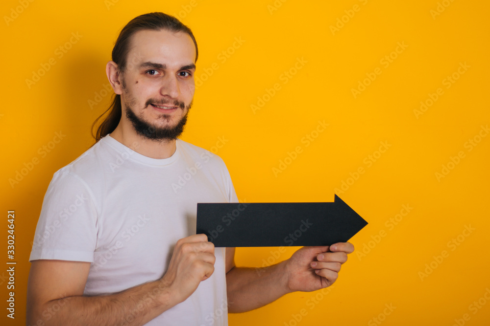 A guy with a beard in a white T-shirt is holding a black tablet in the form of an arrow. A guy with a beard in a white T-shirt is holding a black tablet in the form of an arrow.