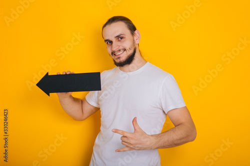 A guy with a beard in a white T-shirt is holding a black tablet in the form of an arrow.