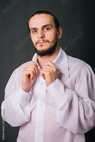 A guy with a beard in a white vintage shirt. Romantic portrait on a gray background