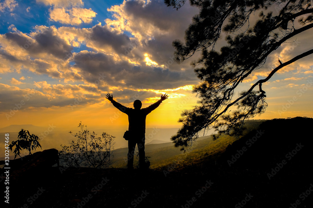 Silhouette of man on cliff in mountains looking into sunset