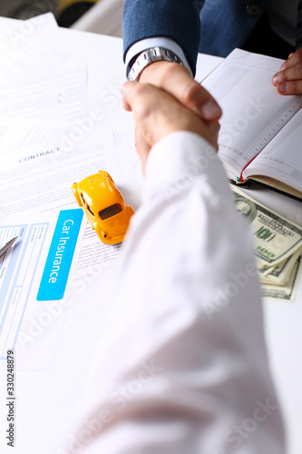 Insurance form lying on table with unrecognizable yellow toy car closeup. Handshake in background. Driver money loss prevention, secure road trip, harmless drive idea, owner protective offer concept