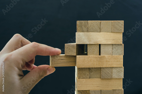 Close up of man's hand take one block to a tower of wooden blocks, dark tone.