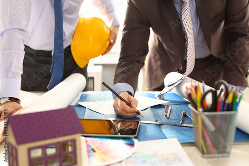 Architect Engineer Team Work on Building Draft. Two Professional Builder Holding Yellow Hardhat Designing House Model on Blueprint Using Pencil. Measuring Tools, Laptop at Workplace