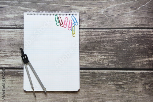 Notepad with a blank white sheet in a checker paper and with compass lies on the background of wooden boards