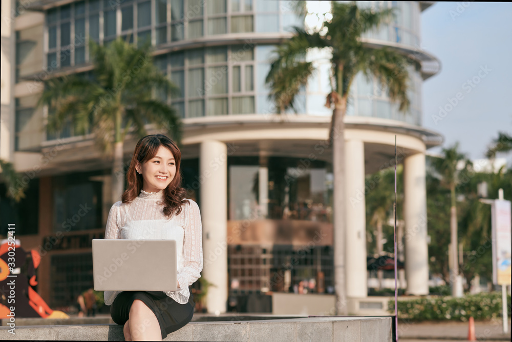 Happy young asian woman working on laptop in the park.