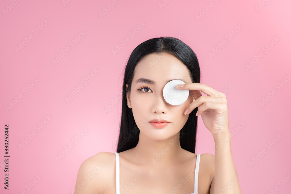 Crop attractive young female cleansing face with a cotton pad on a pink background in studio Crop attractive young female cleansing face with a cotton pad on a pink background in studio