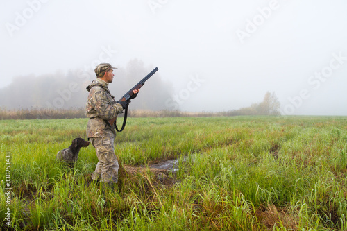 a hunter with a dog stands in a wet meadow
