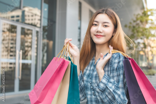 Smiling young Asian woman with shopping colour bags over mall background. using a smart phone shopping online  and smiling while standing mall building. lifestyle concept © anon
