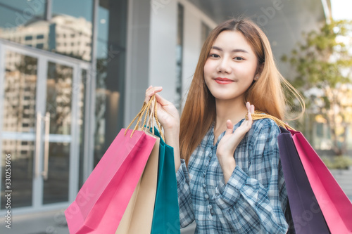 Smiling young Asian woman with shopping colour bags over mall background. using a smart phone shopping online and smiling while standing mall building. lifestyle concept