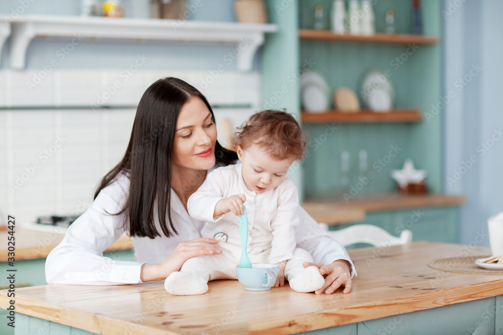 Beautiful young mother communicates and feeds the child in the kitchen at the table
