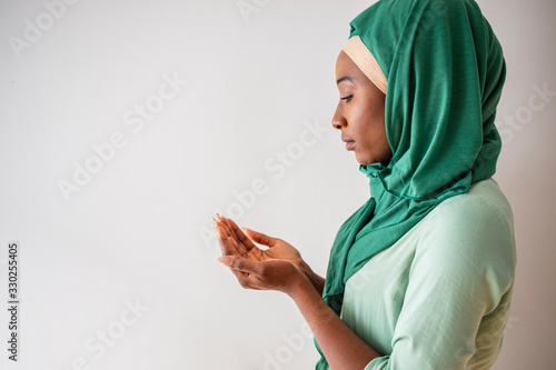 Young muslim woman in green hijab and traditional clothes praying for Allah, copy space. Arab Muslim woman praying, isolated on grey background. Humble Muslim woman holding hands up and praying  photo