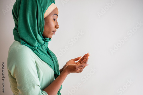 Young muslim woman in green hijab and traditional clothes praying for Allah, copy space. Arab Muslim woman praying, isolated on grey background. Humble Muslim woman holding hands up and praying photo
