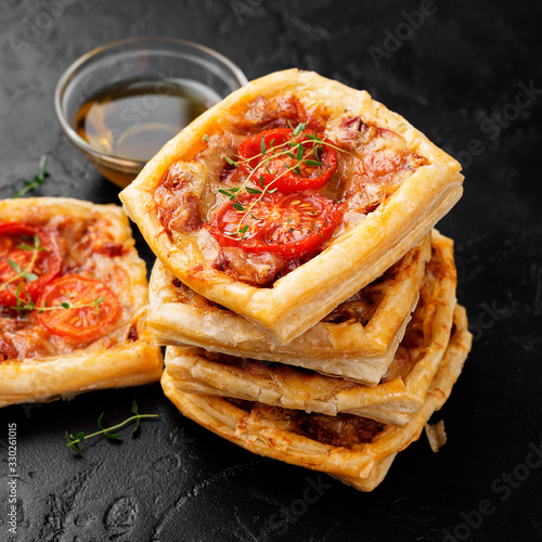 Puff pastry mini pies with cheese and tomatoes on black background