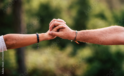 Love and team concept with woman and man hands holding together - help and cooperation people - green defocused background - together forever care each other lifestyle