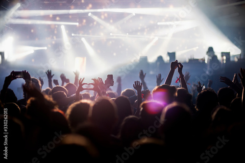 Stage lights and crowd of audience with hands raised at a music festival. Fans enjoying the party vibes.