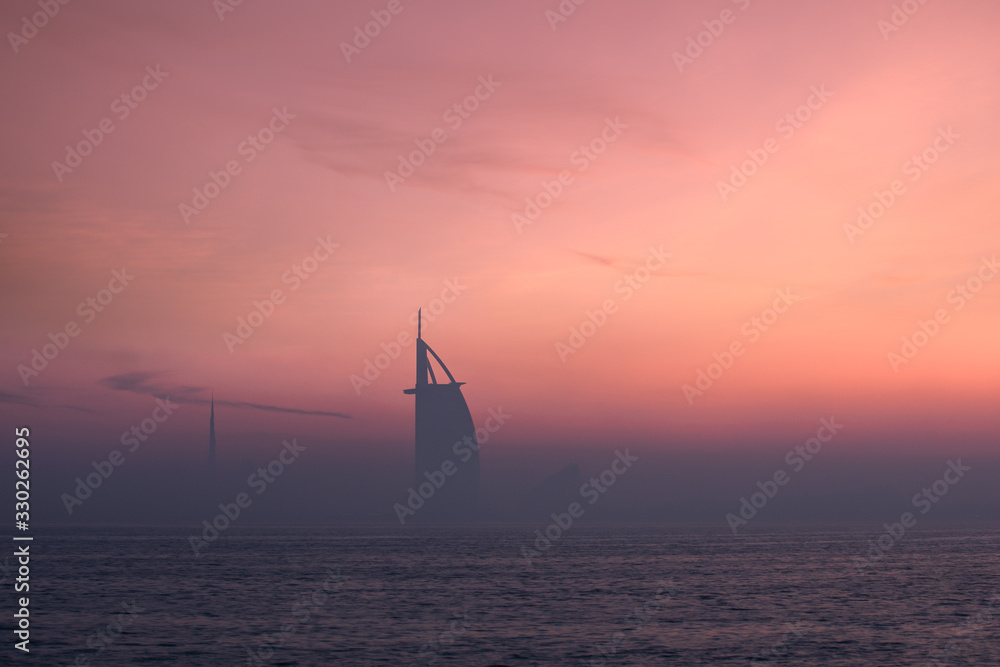 Fototapeta premium Dawn colors over the Dubai Jumeirah disctrict cityscape on a hazy day. Palm Jumeirah, Dubai, United Arab Emirates.