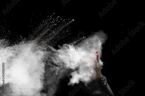 Hand throwing podwer up to the air.Freeze motion of white dust particles splash on black background. photo