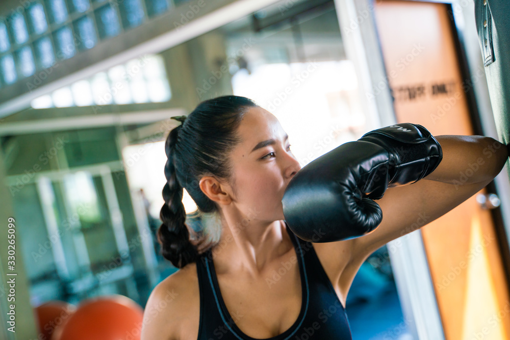 Attractive Asian Female Punching A Black Bag With Boxing Gloves On In Gym