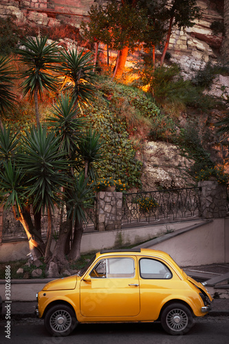 Yellow little retro car on a background of green palm trees in Italy, Sorrento. Concept: a trip on a vintage car along the amalfi coast of Italy. © Natallia