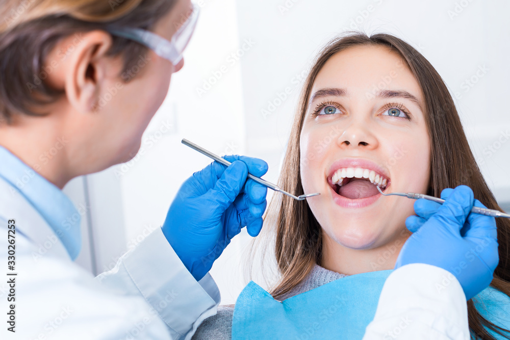 Smiling young woman is sitting in dental blue chair in clinic, office. Man doctor, orthodontist is conducting examination, treating teeth with tools, instruments. Visit to dentist concept. Smiling young woman is sitting in dental blue chair in clinic, office. Man doctor, orthodontist is conducting examination, treating teeth with tools, instruments. Visit to dentist concept.