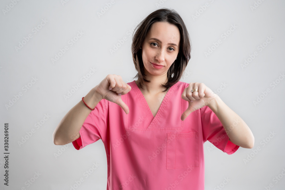 Young woman medical professional nurse or doctor dressed with pink hospital clothes showing double dislike Young woman medical professional nurse or doctor dressed with pink hospital clothes showing double dislike