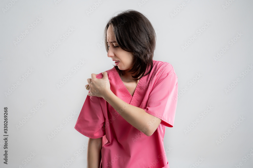 Young woman medical professional nurse or doctor dressed with pink hospital clothes has shoulder pain Young woman medical professional nurse or doctor dressed with pink hospital clothes has shoulder pain