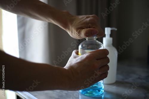 opening alcohol bottle to clean up everything. alcohol bottle and gel dispenser for hands cleaning and sterilization. beating germs bacteria and viruses. getting through co-vid19 outbreak.