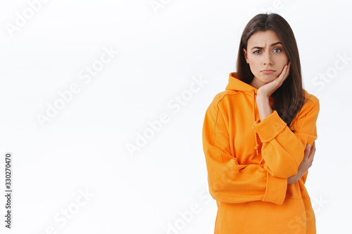 Skeptical and unamused brunette girl hear friends suggestion, looking judgemental and doubtful at camera with raised eyebrow, express disbelief, lean face on hand, standing white background