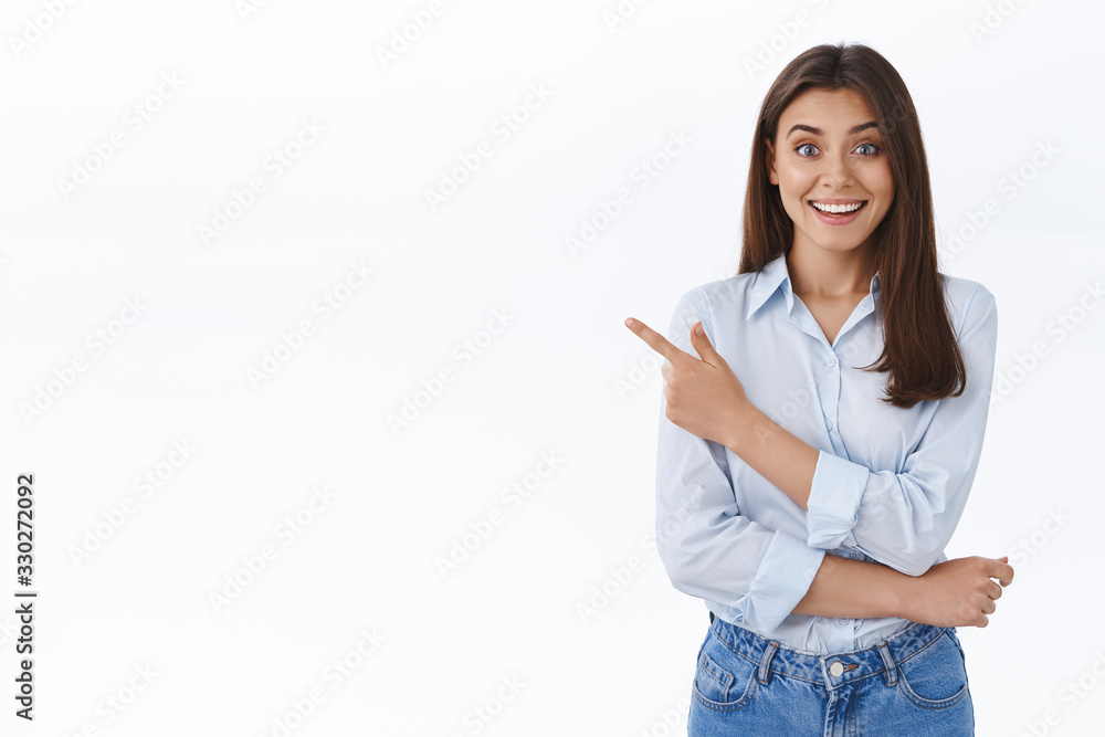 Look here. Impressed and happy cheerful young adult woman in blue blouse, pointing finger left and smiling at camera excited, heard about awesome event nearby, inviting you apply together Look here. Impressed and happy cheerful young adult woman in blue blouse, pointing finger left and smiling at camera excited, heard about awesome event nearby, inviting you apply together