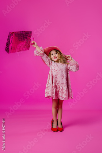 little girl in her mother's big shoes, dress, hat, and shopping bags. baby girl smiling and holding bags from the store. little fashionista on a shopping trip