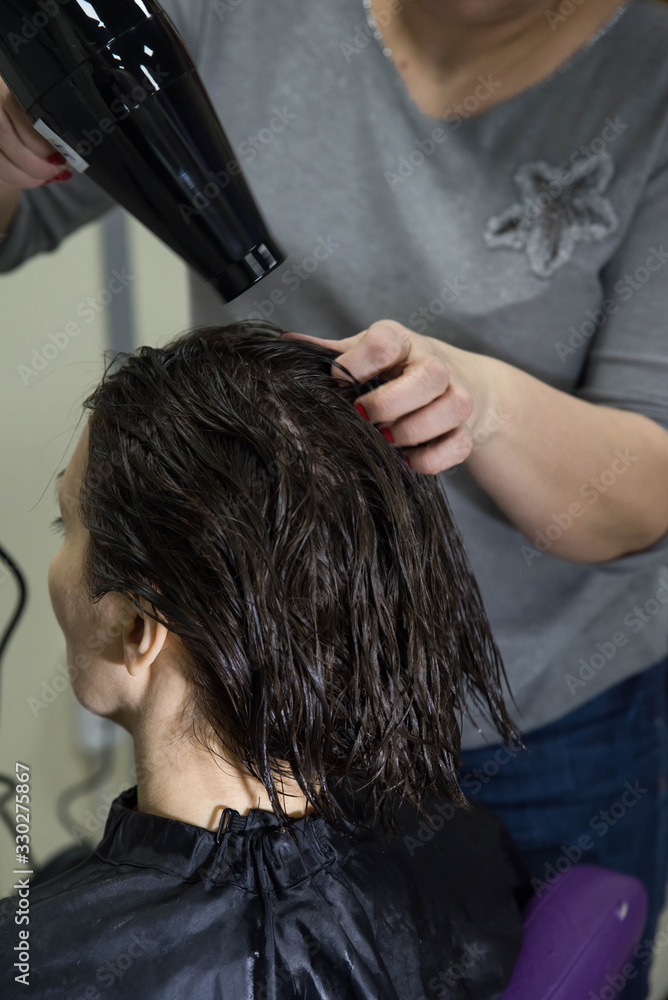 Naklejka premium Professional hairdresser drying woman's hair with hair dryer in beauty salon after beauty procedures and hair coloring