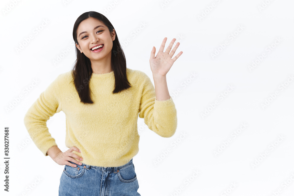 Friendly nice asian woman in yellow sweater greeting friends, waving hand in hi, hello gesture and smiling carefree, welcoming new people to their multicultural team at work, helping out start career Friendly nice asian woman in yellow sweater greeting friends, waving hand in hi, hello gesture and smiling carefree, welcoming new people to their multicultural team at work, helping out start career