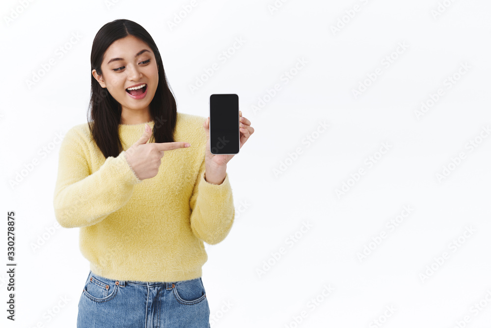 Excited cute girl showing her favorite game on smartphone screen, pointing and showing mobile display with amused cheerful face, smiling upbeat, discuss awesome application, white background Excited cute girl showing her favorite game on smartphone screen, pointing and showing mobile display with amused cheerful face, smiling upbeat, discuss awesome application, white background