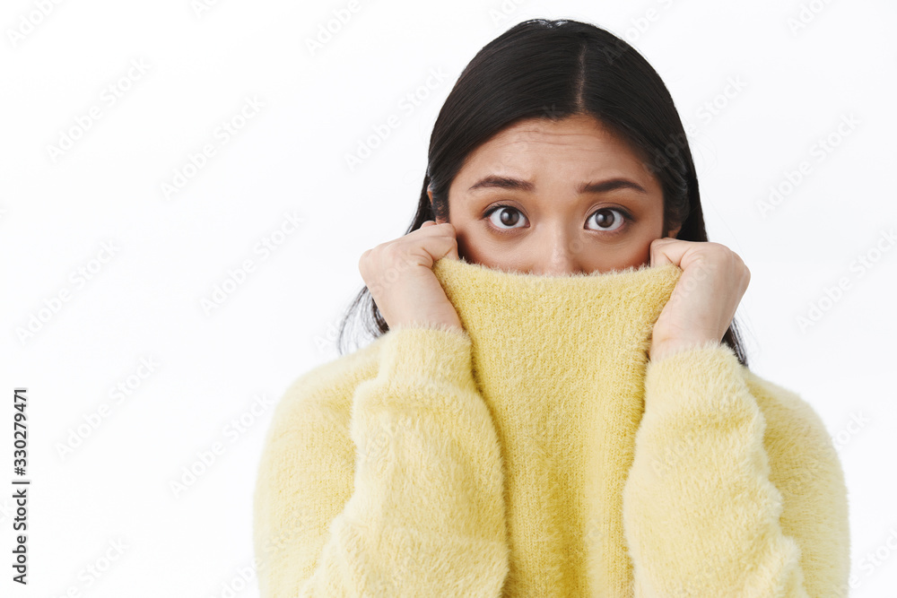 Close-up portrait timid and insecure cute asian girl pull sweater collar on face as feel afraid and scared of horror movie, eyes exress fear, trembling frightened, standing white background - obrazy, fototapety, plakaty 