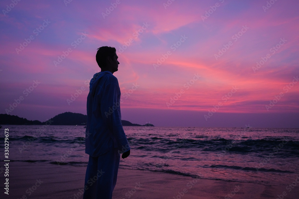 A man practices yoga on the ocean during a purple sunset.