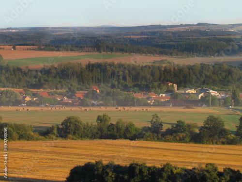 Fototapeta Naklejka Na Ścianę i Meble -  Hilly landscape in early evening at the end of summer, light haze of fog around village in valley, plowed fields, Central Bohemia region