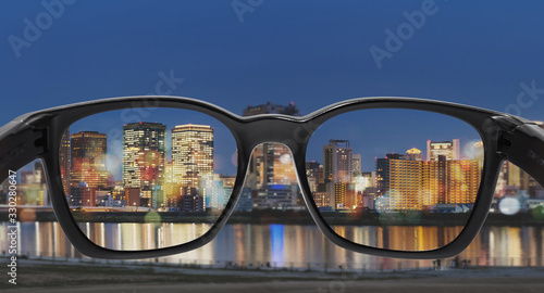 Looking through eyeglasses to city at night, focused on lens with blurry background