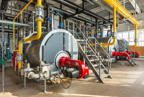 The interior of an industrial boiler room with three large boilers, many pipes, valves and sensors photo
