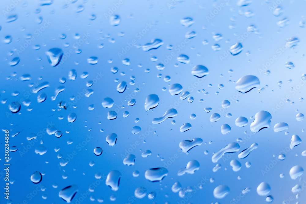 Wet glass with rain drops on blue sky background_